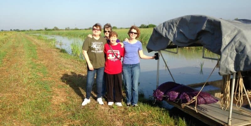 Four women pose together on a grassy bank beside a body of water. Four women pose together on a grassy bank beside a body of water.
