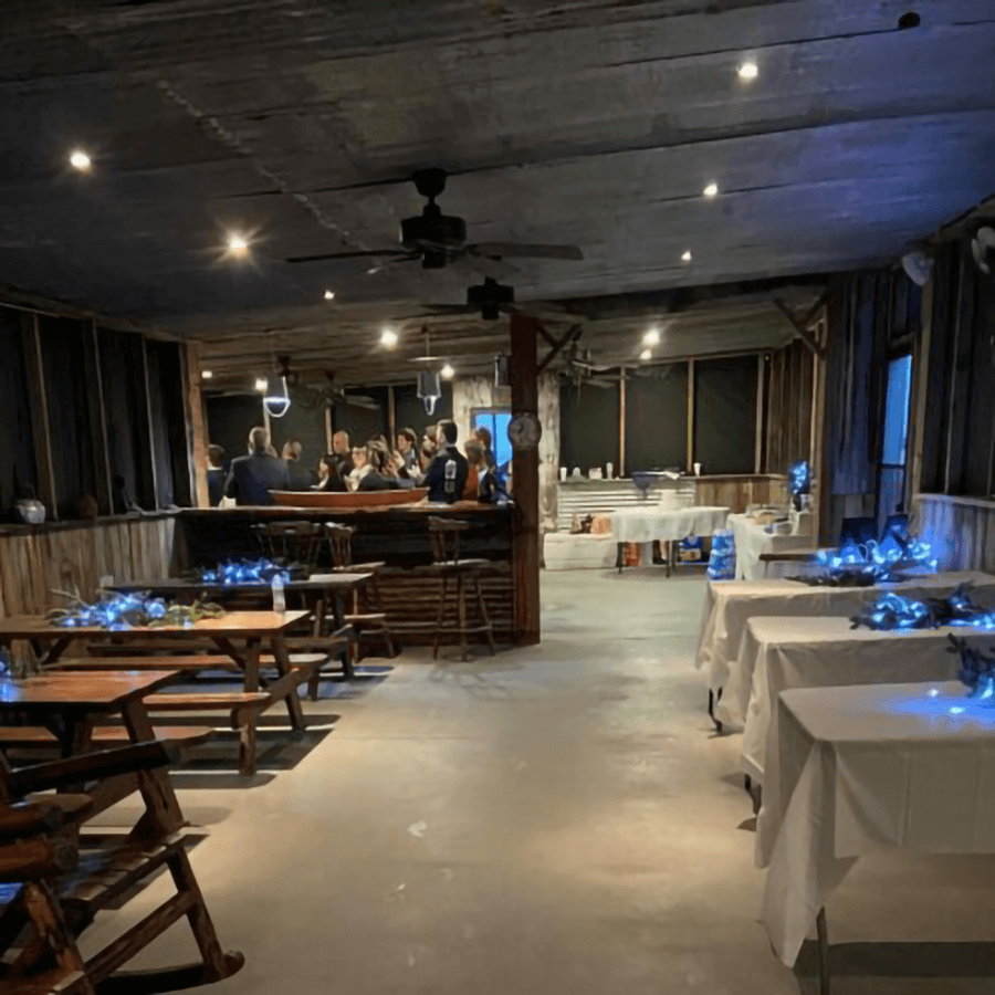 An inviting, rustic event space with table settings and a gathering of people at the bar.