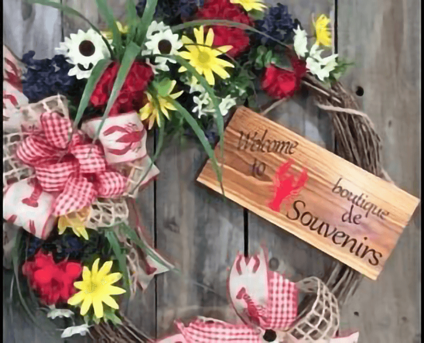 A decorative wreath featuring flowers and a wooden sign that reads "Welcome to boutique de Souvenirs."