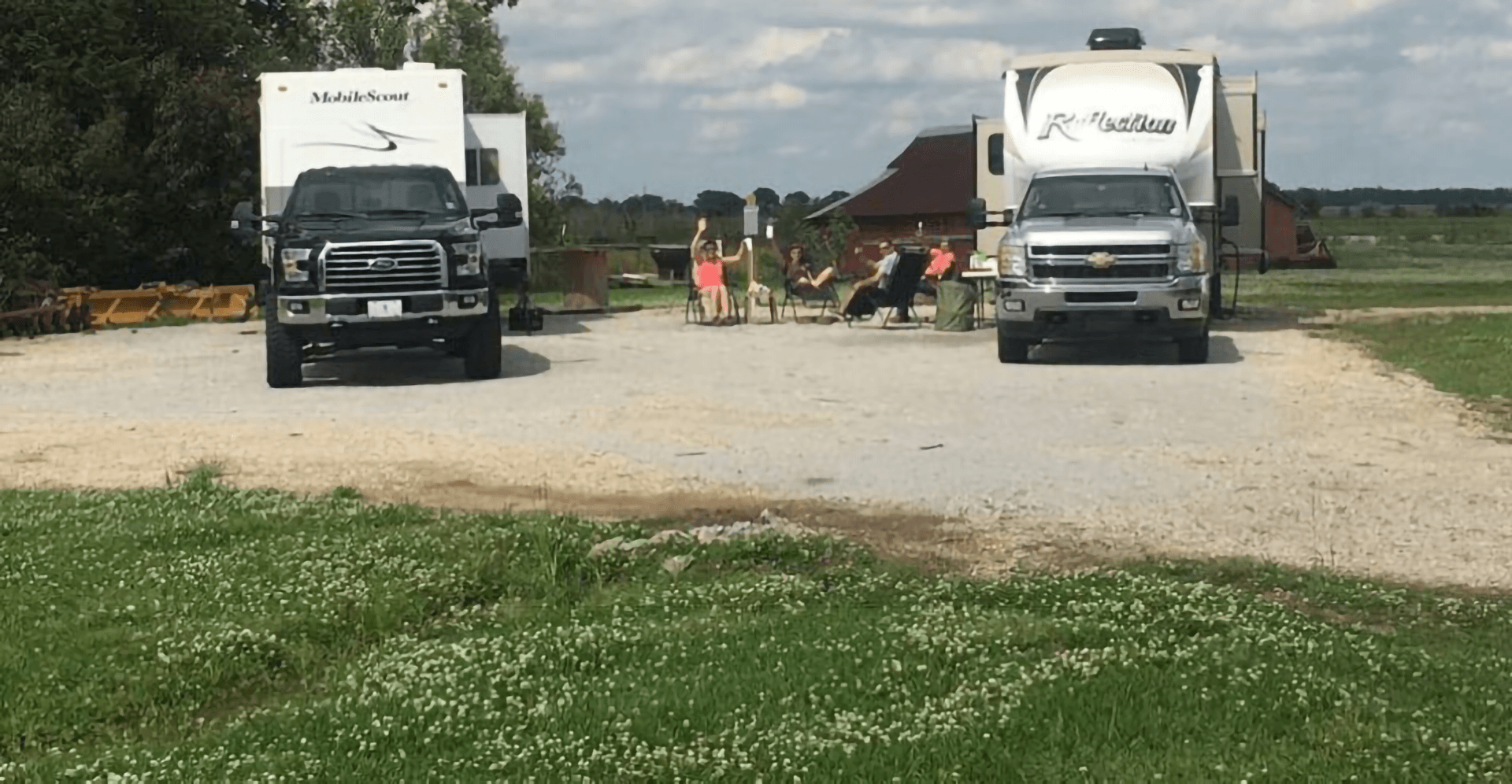 Two RVs parked side by side with people sitting on chairs in between, enjoying the outdoors.