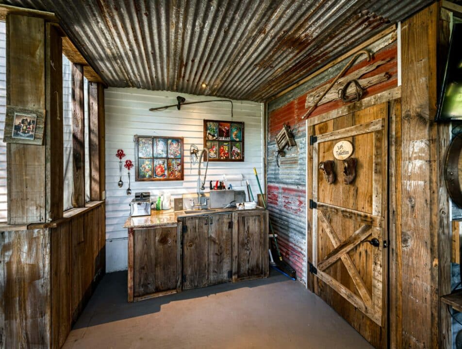 A rustic kitchen with wooden cabinetry and corrugated metal accents, featuring floral decor and an open door.