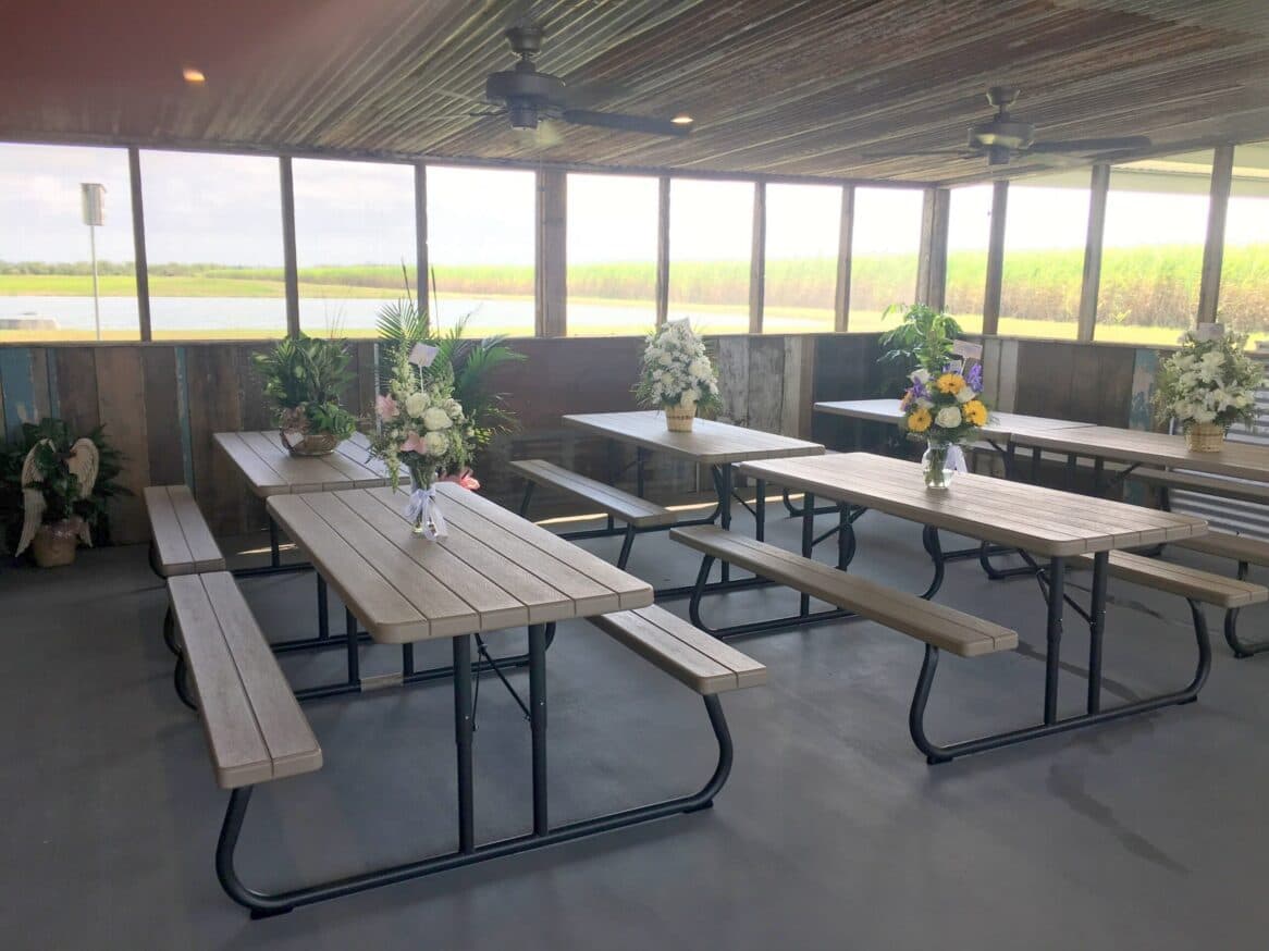 Indoor seating area with wooden picnic tables and flower arrangements, overlooking a green landscape.