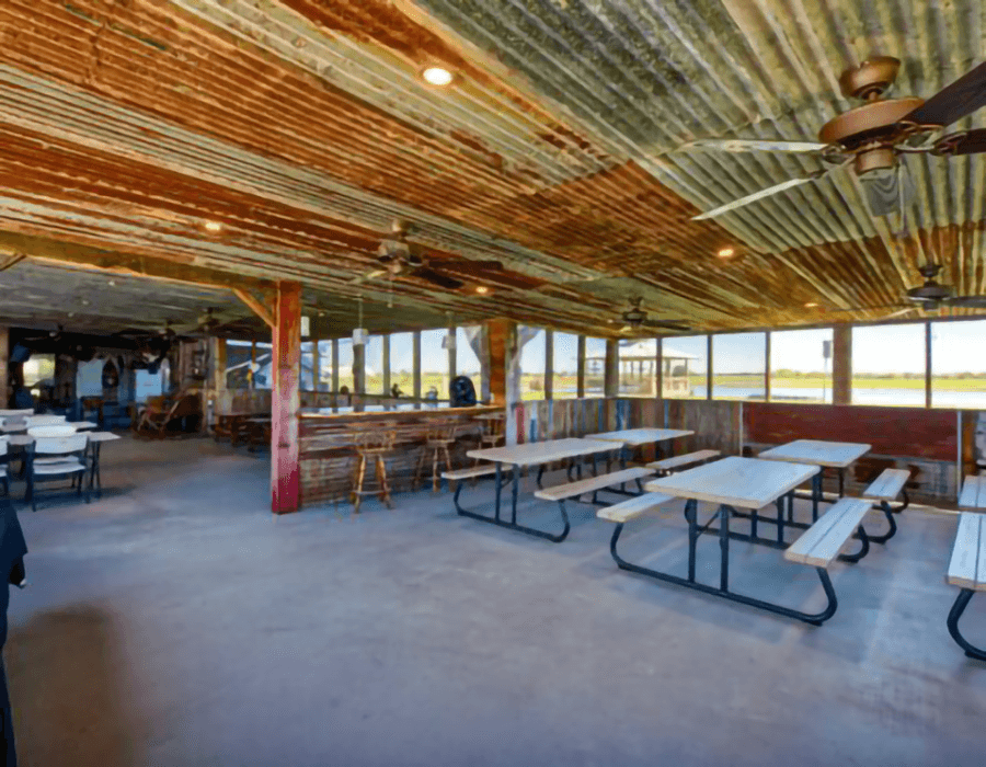 Interior of a rustic dining space with metal roofing, wooden furnishings, and large windows overlooking a scenic view.
