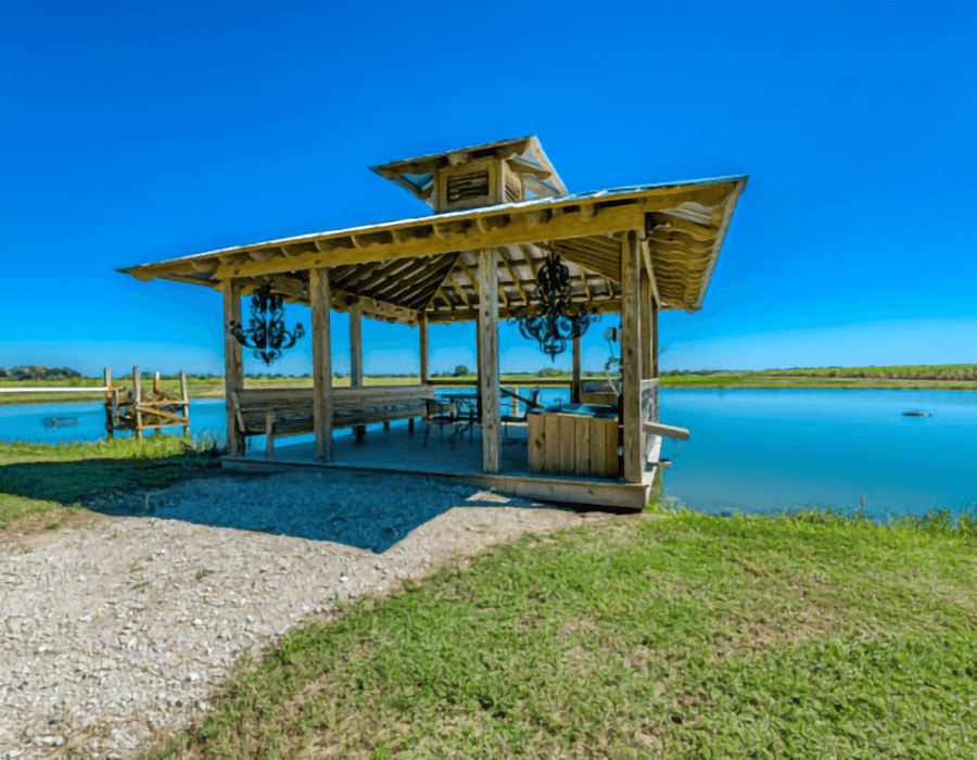 A wooden gazebo by a tranquil lake under a clear blue sky.