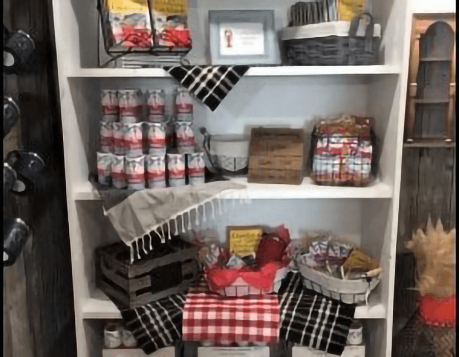 A display shelf filled with various canned goods, baskets, and decorative items, arranged with checkered fabric accents.