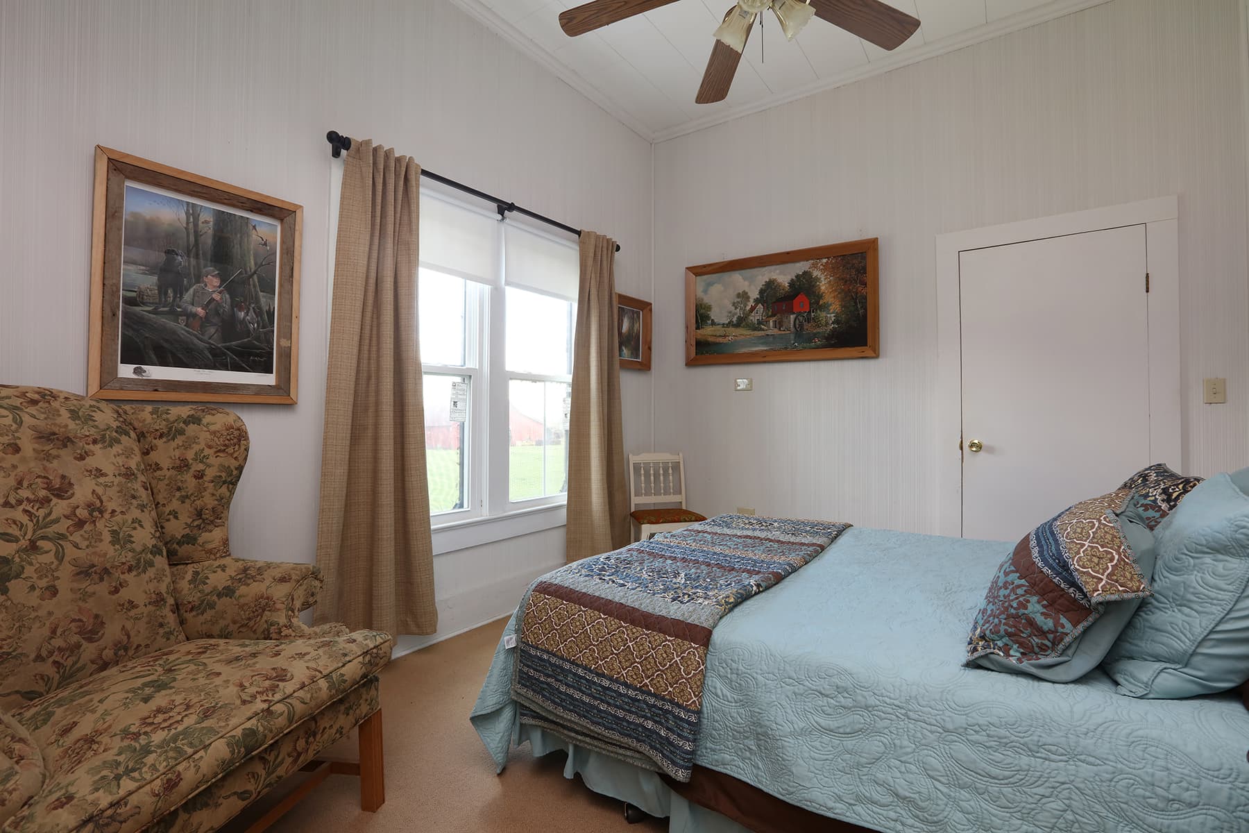 Cozy bedroom featuring a light blue bedspread, patterned pillows, and a comfortable armchair beside a window.