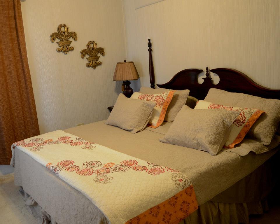 A cozy bedroom featuring a neatly made brown bed with patterned pillows, a decorative quilt, and elegant wall accents.