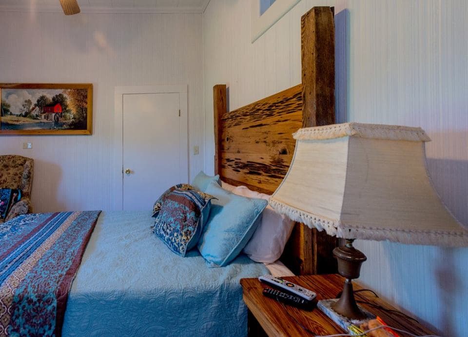 Cozy bedroom featuring a large wooden headboard, light blue bedding, a bedside lamp, and artwork on the wall.