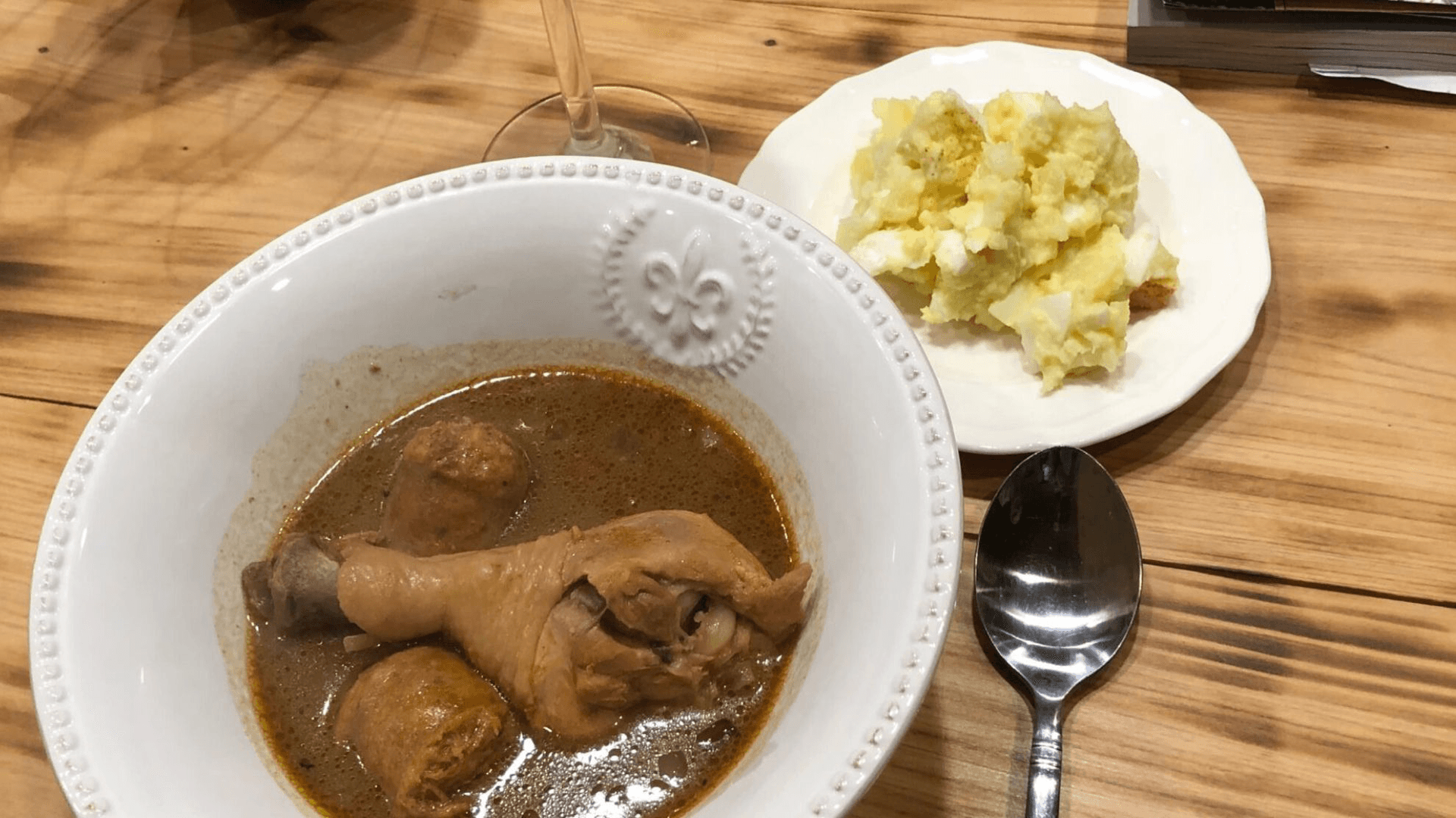 A bowl of chicken curry with meatballs alongside a plate of mashed potatoes on a wooden table.