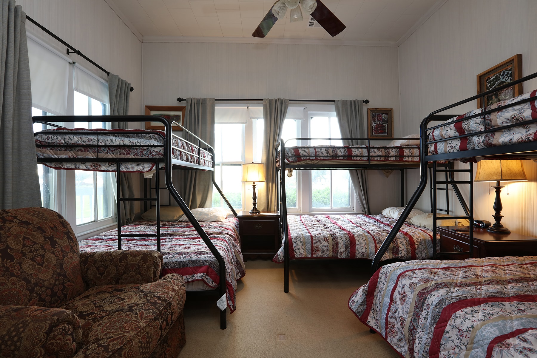 A cozy bedroom featuring two sets of bunk beds, a single bed, and a comfortable chair by the window.
